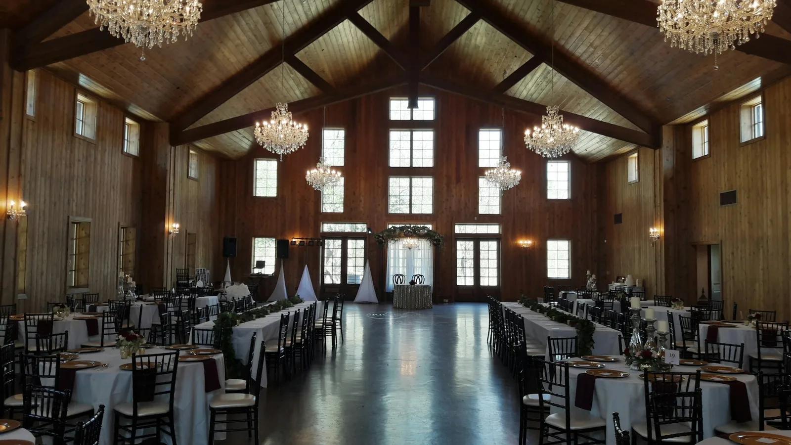 Une grande salle vide sous une charpente en bois, avec des tables dressées des deux côtés et une piste de danse au milieu