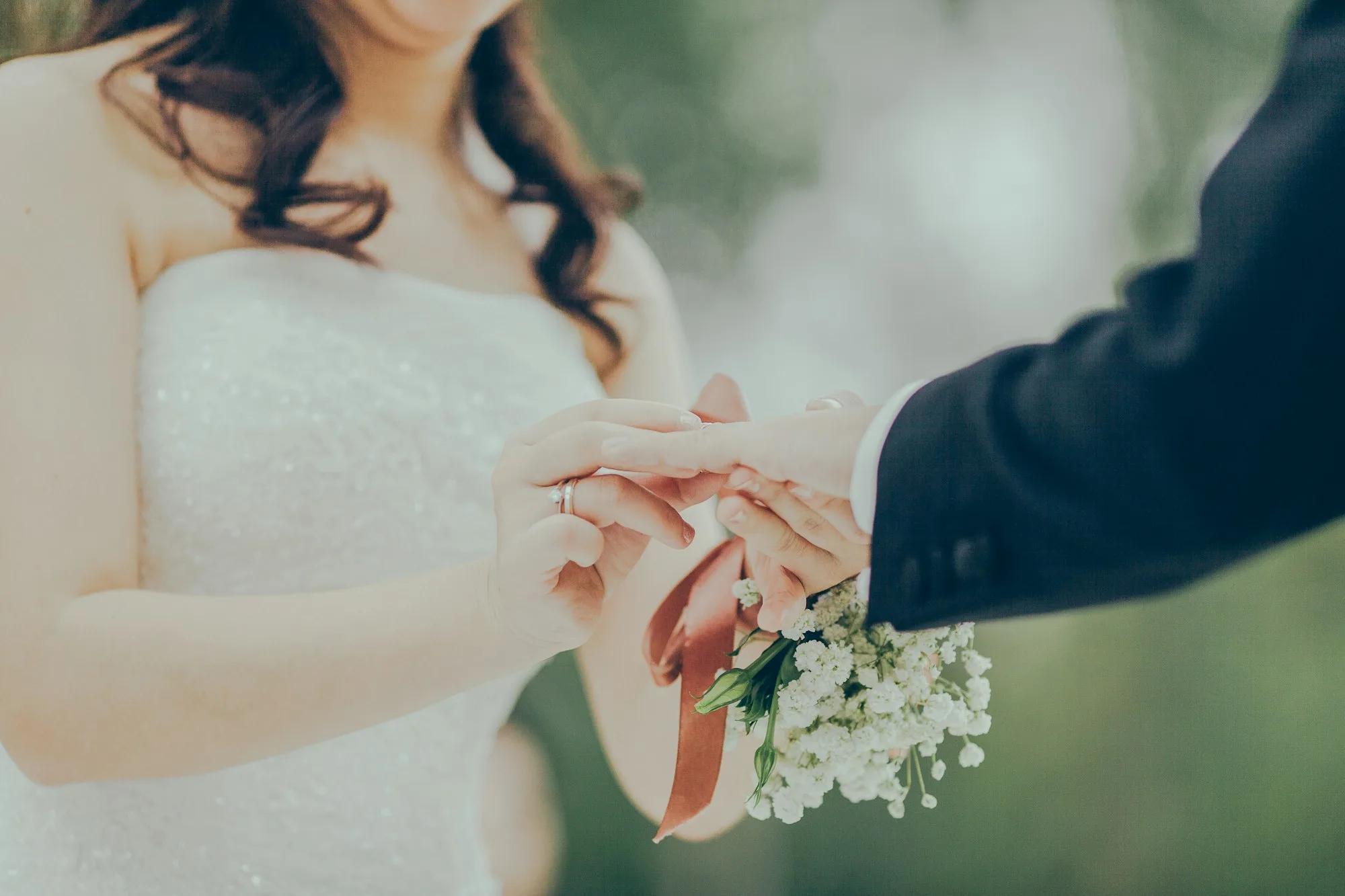 عروس تُلبس شريكها خاتم الزواج، إلى جانب باقة صغيرة من زهور الجبسوفيلا مربوطة بشريط بلون الصدأ
