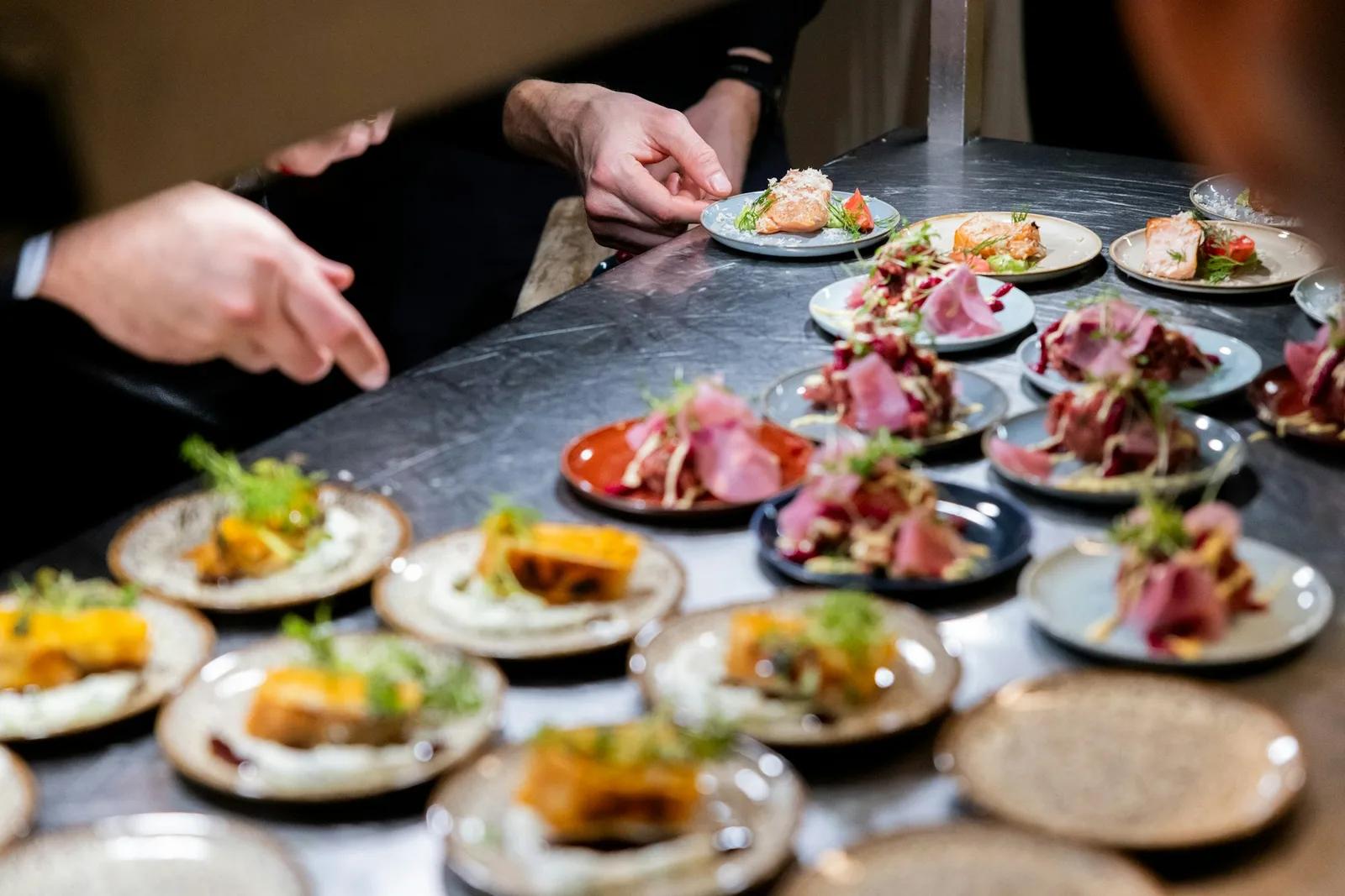 Des mains de cuisiniers finissent des rangées de petites assiettes d'entrée sur un plan de travail sombre