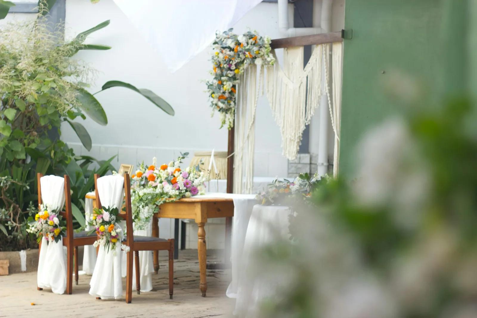 Trautisch mit Blumen, zwei Kerzen und zwei geschmückten Stühlen vor einem Makramee-Vorhang
