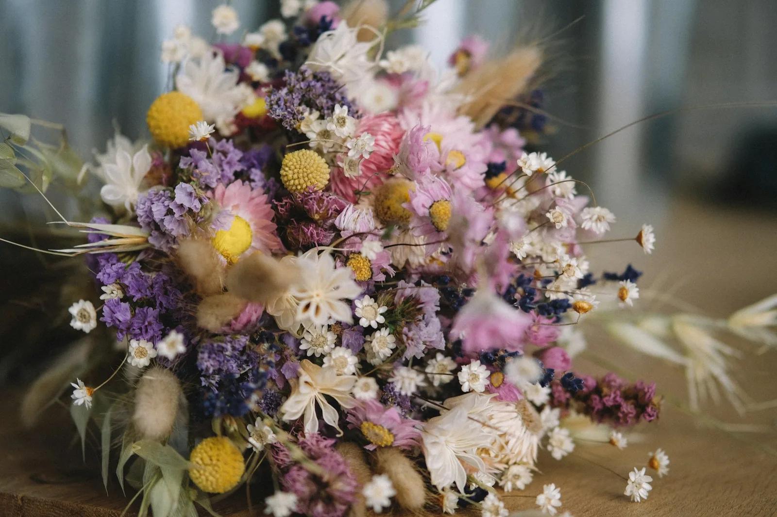 A dried-flower bouquet of billy buttons, statice, strawflowers, lavender and bunny tails on a wooden table